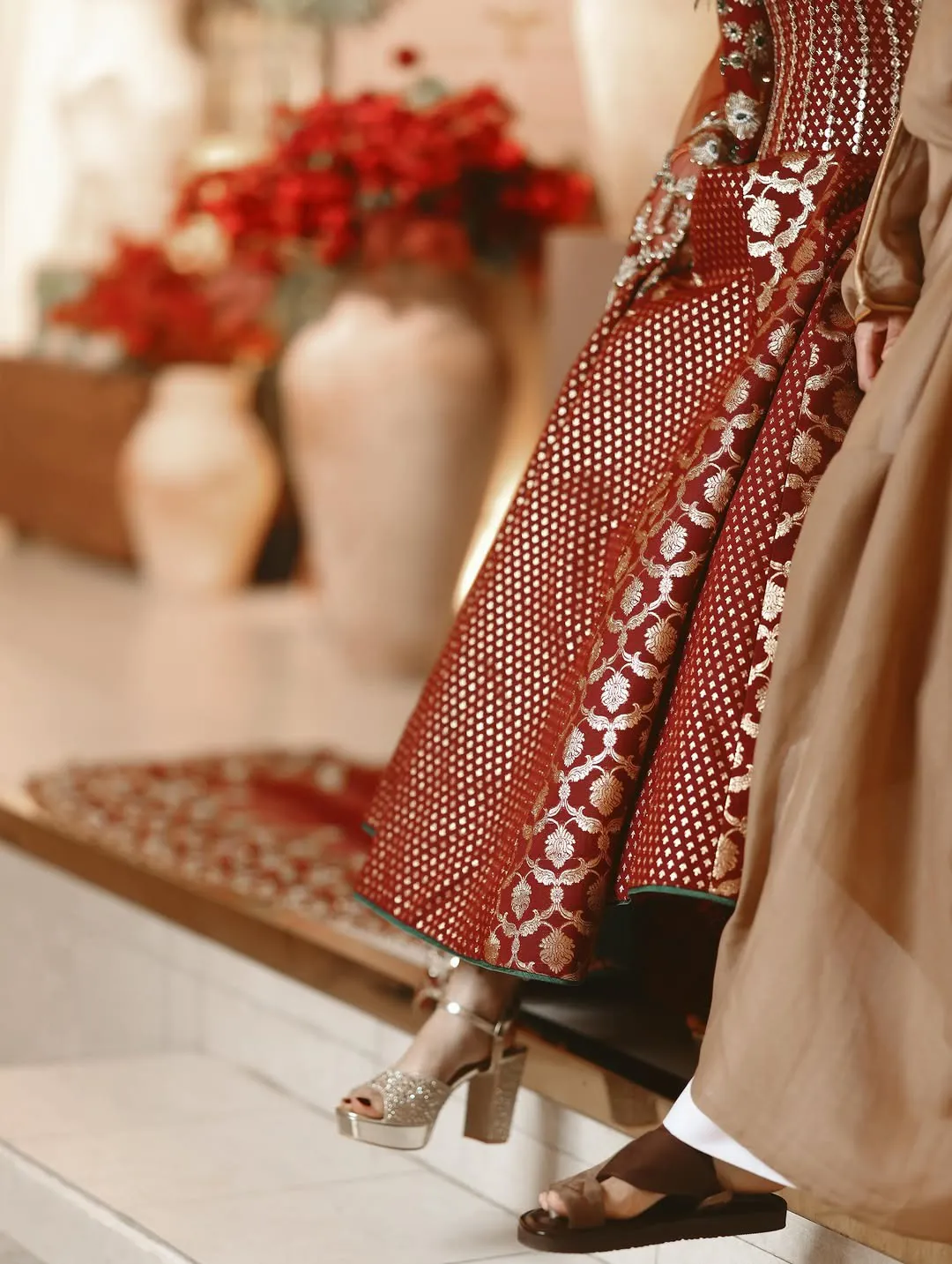 A bride in a red and gold gown and a groom in a bisht stepping down together