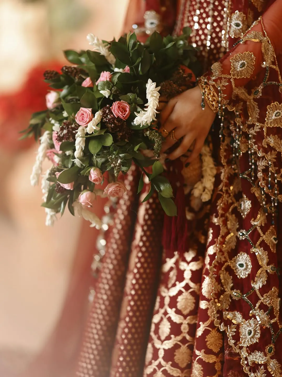 A bride holding pink roses and jasmine against her embroidered gown