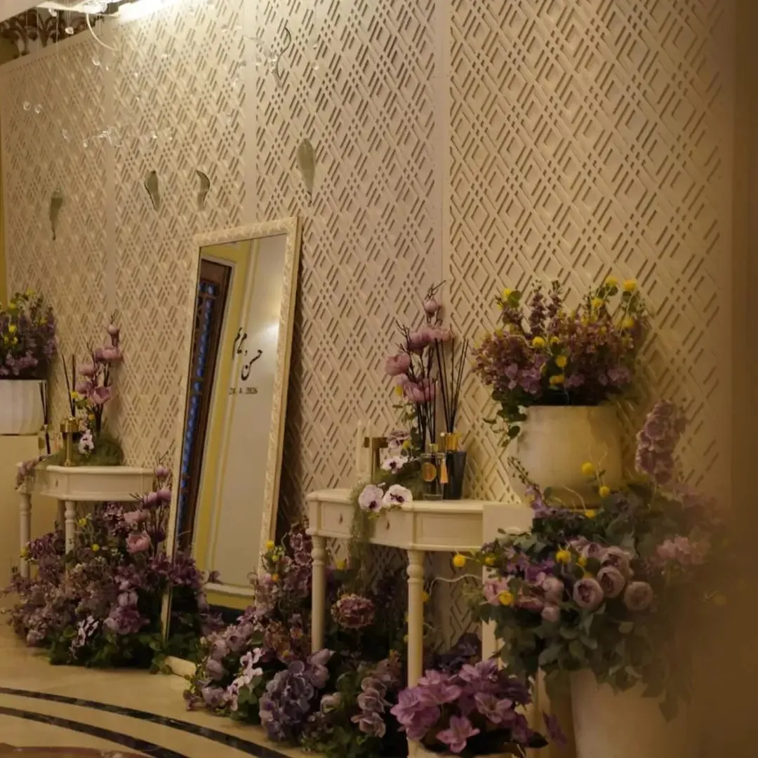 A lattice wall with a mirror and lavender arrangements on off-white consoles