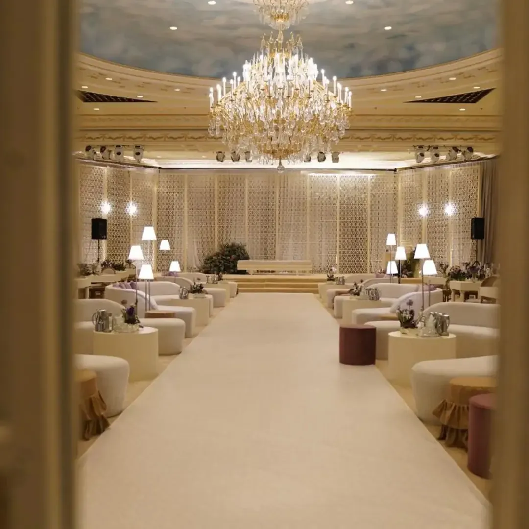 A ballroom set with a white aisle, off-white sofas, small lamps and a crystal chandelier