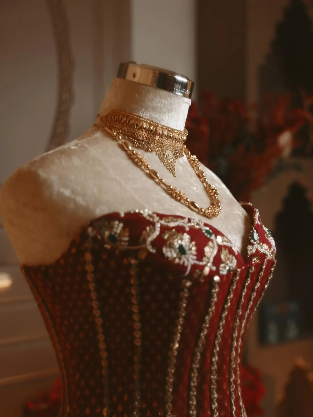 An embroidered red bodice on a dress form with layered gold necklaces