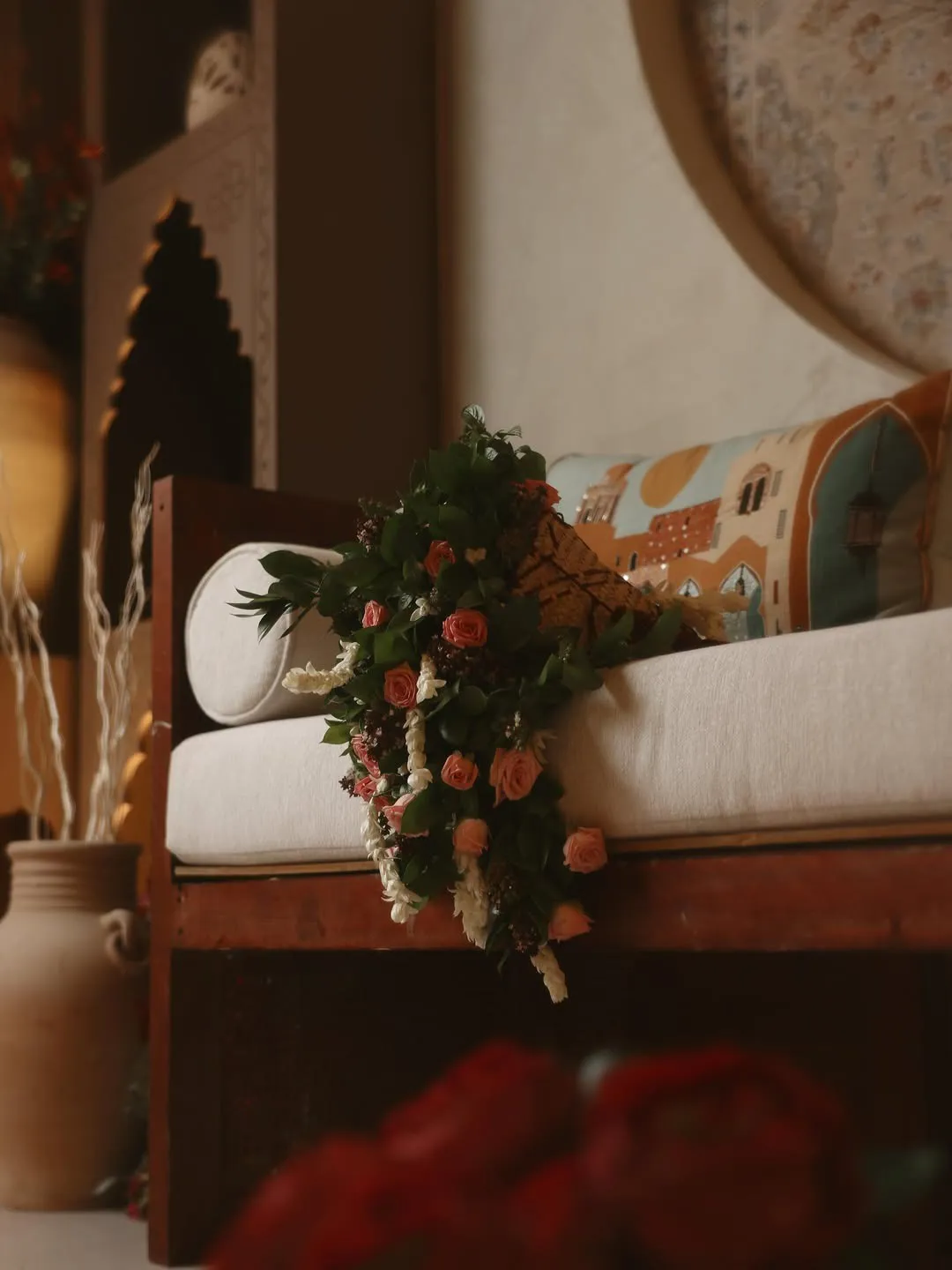 A wooden majlis daybed with white cushions and a rose and jasmine bouquet